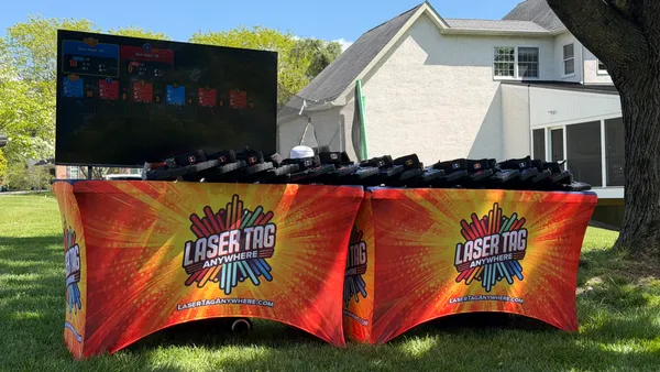 Pro-grade Laser Tag Anywhere equipment table with branded covers, taggers, and a live TV scoreboard at a backyard event