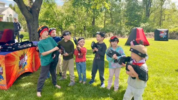 Little boy cracking up mid-game as a teen player aims back at him during a backyard laser tag birthday in Glen Mills, PA