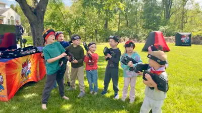 Little boy cracking up mid-game as a teen player aims back at him during a backyard laser tag birthday in Glen Mills, PA