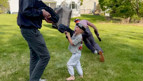 Kid going prone in the grass to flank opponents while the adults sprint behind him at a Glen Mills, PA laser tag party