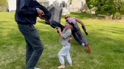 Kid going prone in the grass to flank opponents while the adults sprint behind him at a Glen Mills, PA laser tag party