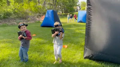 Two boys laughing as they aim laser taggers at an outdoor birthday party in Glen Mills, Delaware County, PA