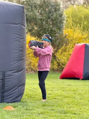 Young girl mid-game with a laser tagger between inflatable bunkers at an 8 year old's backyard birthday party
