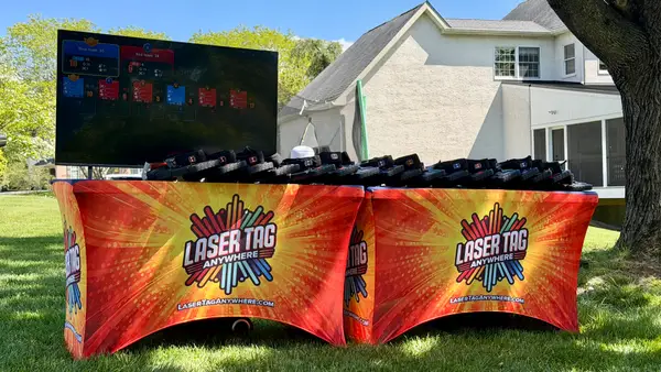 Pro-grade Laser Tag Anywhere equipment table with branded covers, taggers, and a live TV scoreboard at a backyard event