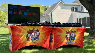 Pro-grade Laser Tag Anywhere equipment table with branded covers, taggers, and a live TV scoreboard at a backyard event