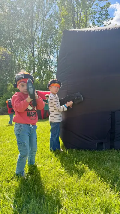 Two young boys in headbands aiming laser taggers around an inflatable bunker at a Glen Mills, PA birthday party