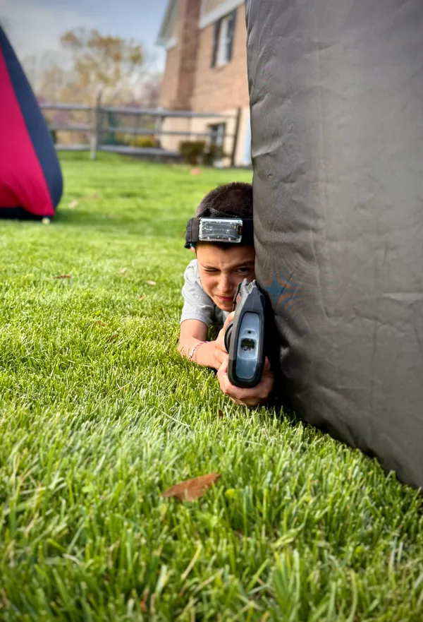 Tactical kid eyeing his next target from behind an inflatable bunker at a backyard mobile laser tag birthday party