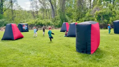 Kids chasing each other across an outdoor inflatable bunker arena at a laser tag party in Delaware County, PA