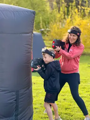 Mom and kid teaming up around an inflatable bunker at an 8 year old's backyard mobile laser tag birthday party