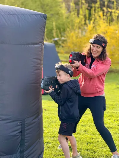 Mom and kid teaming up around an inflatable bunker at an 8 year old's backyard mobile laser tag birthday party
