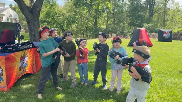 Little boy cracking up mid-game as a teen player aims back at him during a backyard laser tag birthday in Glen Mills, PA