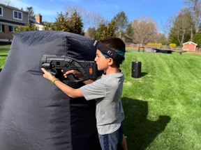 Boy aiming a pro-grade laser tagger around an inflatable bunker at a backyard kids' birthday party in Pennsylvania
